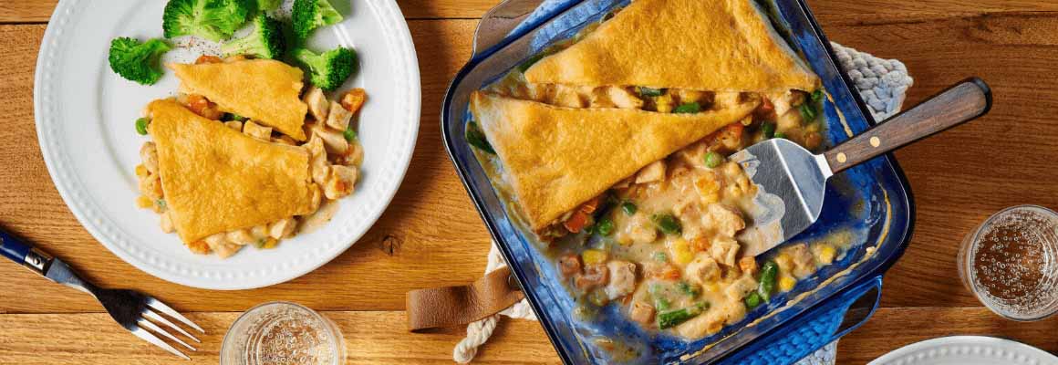 Overhead shot of a creamy chicken pot pie topped with golden pastry, served on a plate with broccoli.