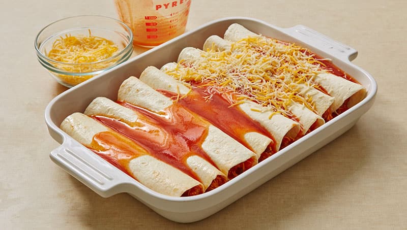 Pour enchilada sauce and shredded cheese over enchiladas.